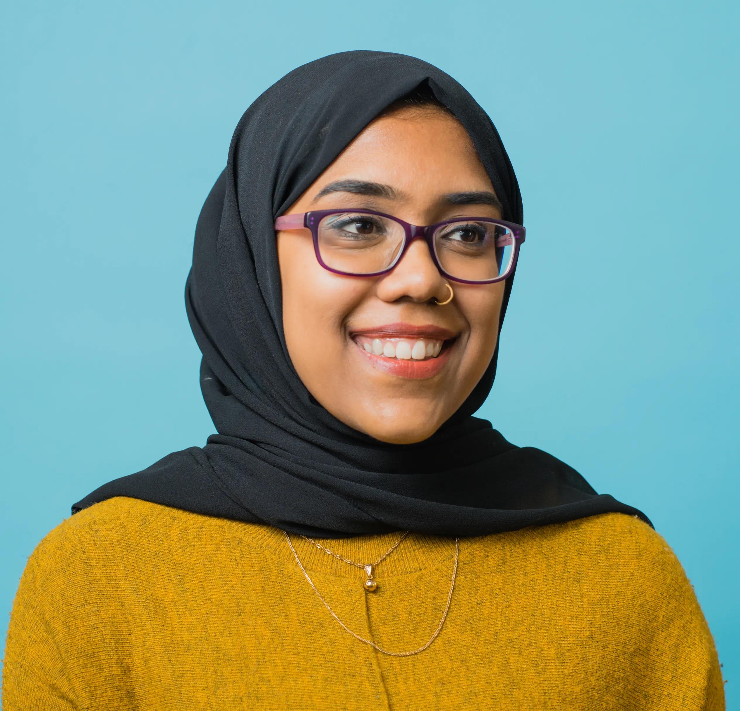 university student in a hijab smiling with a blue background