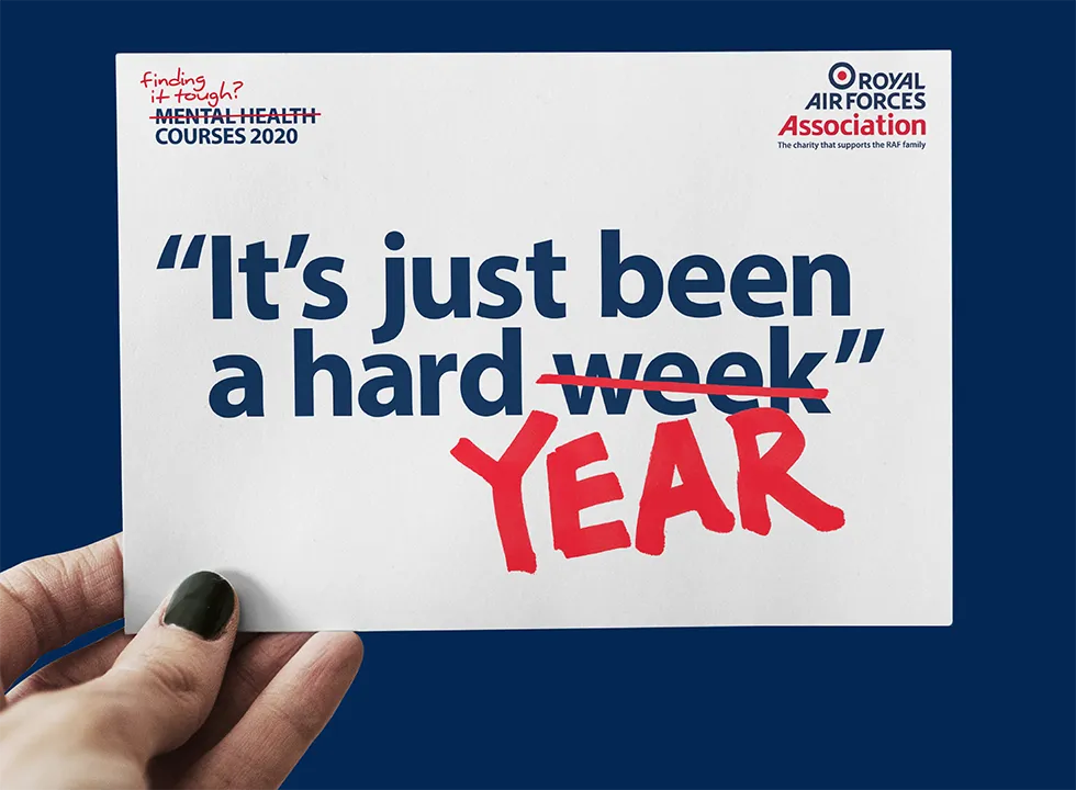 Person holding a postcard with the text 'it has been a hard week' with week crossed out and replaced with year